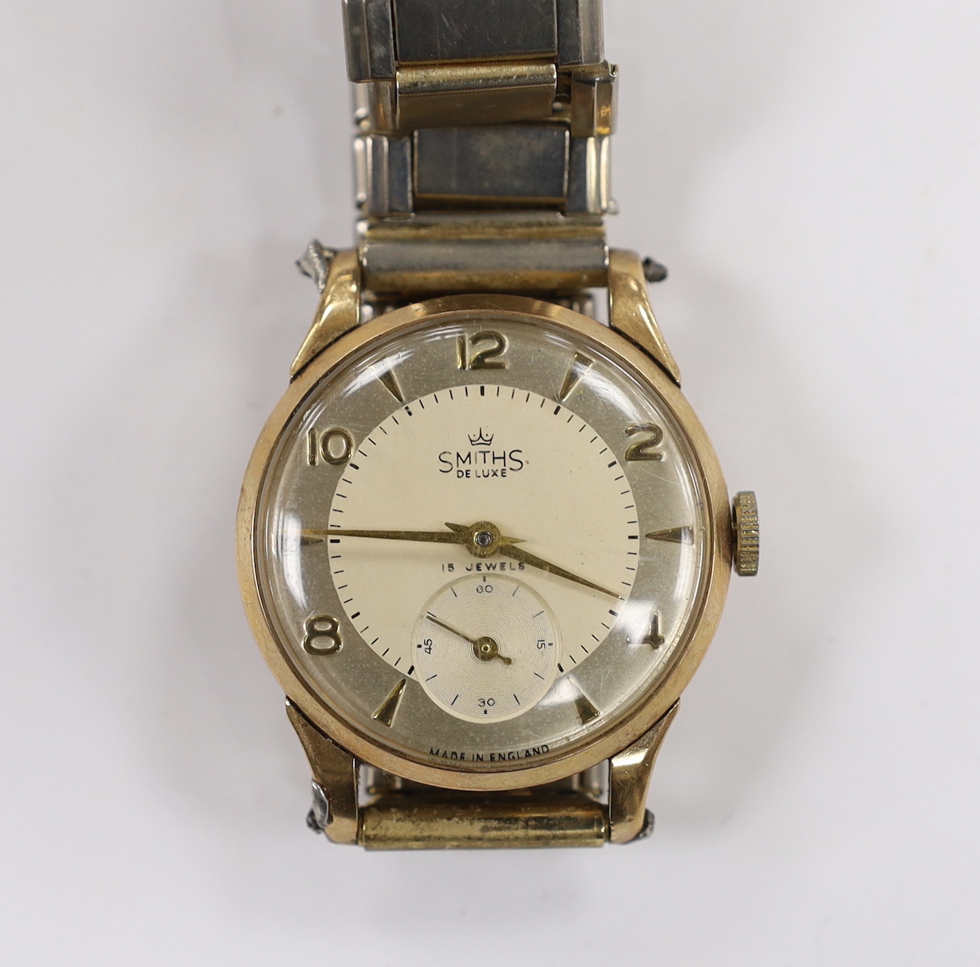 A gentleman's 9ct gold Smiths Deluxe manual wind wrist watch, with subsidiary seconds and case back inscription, on an associated flexible strap.